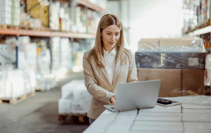 woman in a light colored blazer with silver laptop in a warehouse